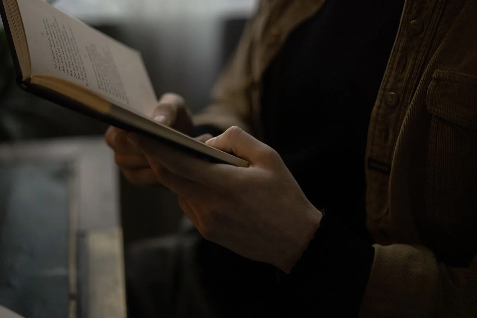 Person holding an open book in a cozy, moody setting